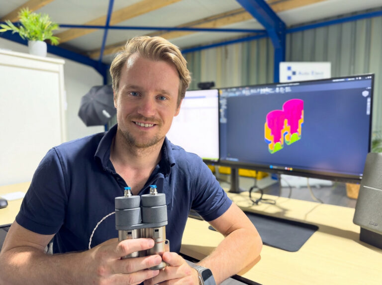 Glenn Roozing, MSc Mechanical Engineer, met een maatwerk batterijconnector-fixture en CAD-ontwerp op de achtergrond.